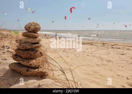 A selective focus shot of stacked stones on a sandy beach with kitesurfers in the background Stock Photo