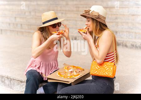 Friends eating pizza in the city enjoying the holidays, sitting on a staircase with the pizza Stock Photo