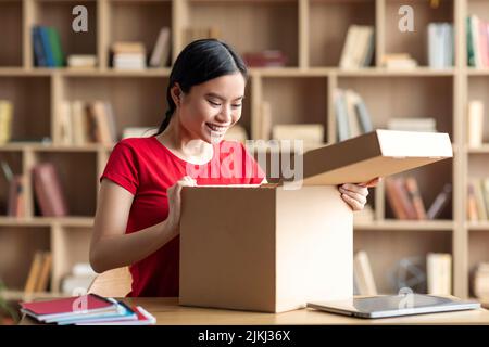 Inspired happy young asian female opens cardboard box, enjoy online shopping and huge sale Stock Photo