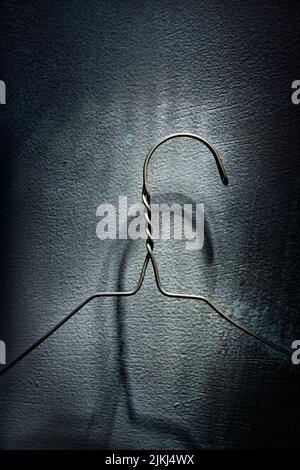A vertical shot of an old metal wire coat hanger casting an ominous shadow on a concrete wall Stock Photo