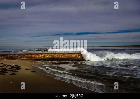 A view of the sea wall getting hit with a big wave at the children's pool in La Jolla California Stock Photo