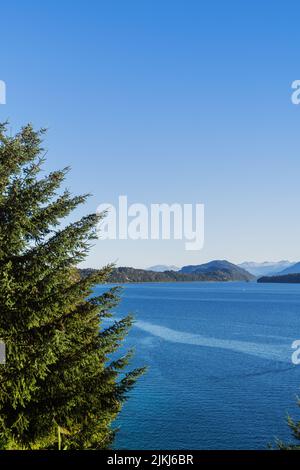 A beautiful tree on the left by the lake with rocky cliffs and mountains on the background Stock Photo