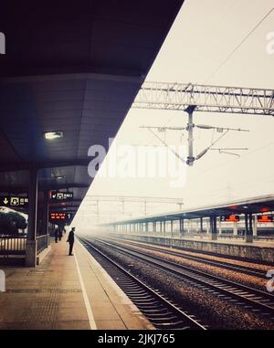 A vertical shot of a man waiting for the train alone at the railway station on a foggy day Stock Photo
