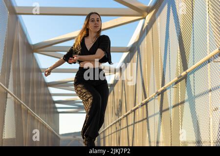 portrait of a young caucasian woman dancing urban dance at sunset on a bridge. waacking dance style Stock Photo
