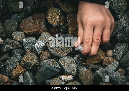 A closeup shot of an adult hand picking up a small gravel off the ground during daytime Stock Photo