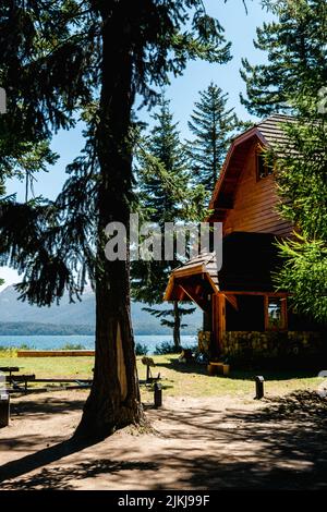 A vertical shot of a wooden house surrounded by greenery and a lake in the background Stock Photo