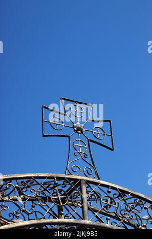 A low angle shot of an iron cross against blue sky in bright sunlight Stock Photo