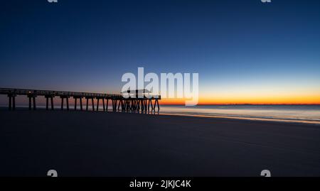 A silhouette of beautiful bridge on the beach with sea under sunset Stock Photo