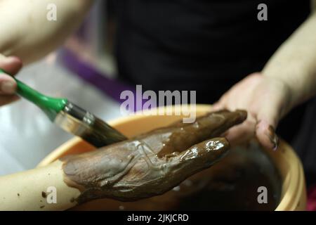 A closeup of a woman's hand undergoing paraffin wax therapy using brown wax Stock Photo