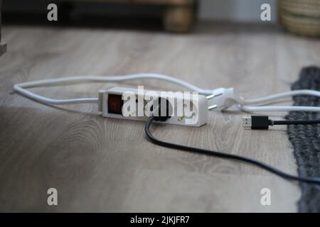 A white extension cord on the room floor connected to other black wires Stock Photo