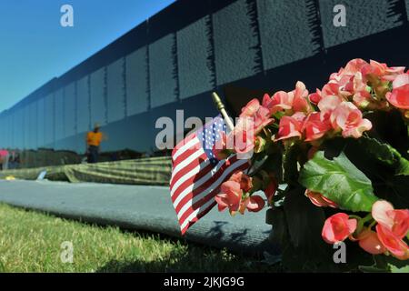 A shallow focus shot of the US flag and flowers in front of the Vietnam Veterans Memorial wall Stock Photo