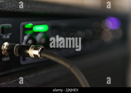 Cable from a bass connected to the amp where you can see some lights and knobs to control the sound. Stock Photo