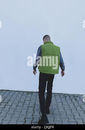 attractiveyoung man model in green gilet and black boots posing next to white wall Stock Photo