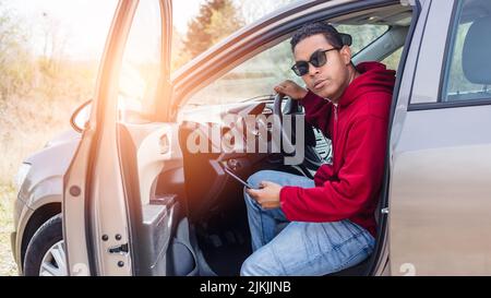 handsome young Hispanic using his car and looking at his smart phone Stock Photo