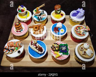 A closeup shot of artistic cupcakes with miniature food toppers on  a wooden board Stock Photo
