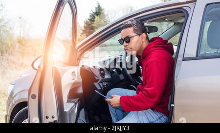 handsome young Hispanic using his car and looking at his smart phone Stock Photo