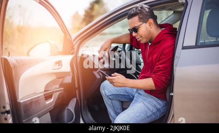 handsome young Hispanic using his car and looking at his smart phone Stock Photo