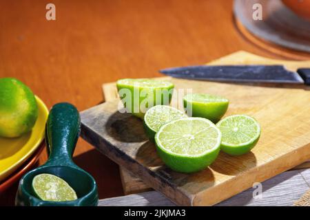 A close-up shot of some sliced limes on a cutting board next to a sharp knife and squizzer. Stock Photo