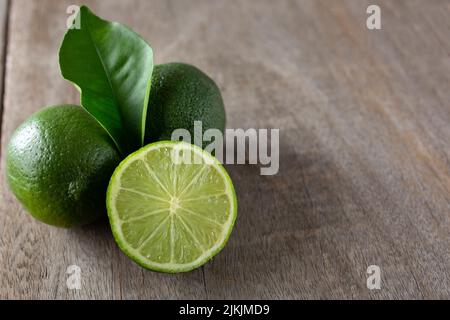 A composition of whole and sliced lime fruits with leaves, on a wooden table Stock Photo