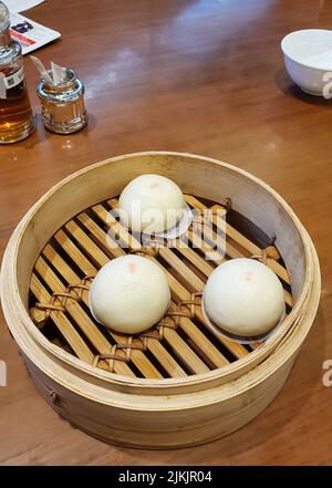 A vertical closeup of Dim sum with Lotus seed buns in a traditional steaming basket. Hong Kong. Stock Photo