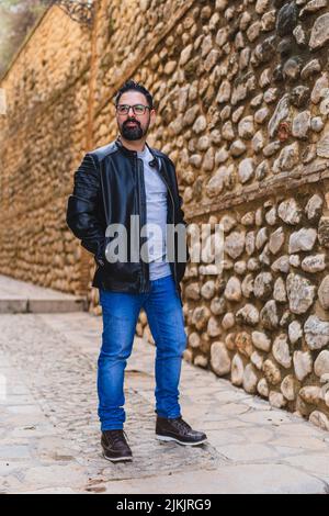 A vertical shot of a handsome man with a beard and glasses posing on a stone wall background Stock Photo