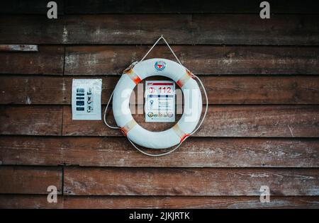 A white lifebuoy ring with a rope hanging against a wooden wall Stock Photo