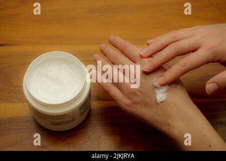 Woman applies hand cream to her hand on wooden isolated background Stock Photo