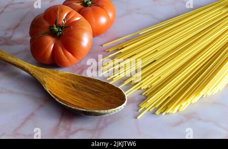 A wooden spoon, spaghetti, red tomatoes, on marble background - ingredients for pasta in the kitchen Stock Photo
