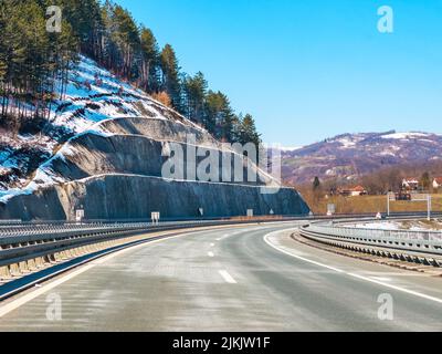 An empty road surrounded by snowy hills on a sunny day Stock Photo