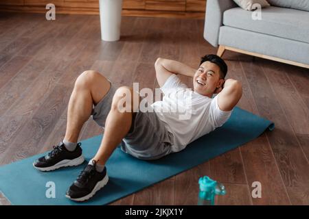Full length of active middle aged man strengthening core muscles, doing abs exercises at home on yoga mat Stock Photo
