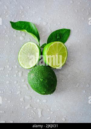 A top shot of fresh green lemon with green leaves on a white table with water drops Stock Photo