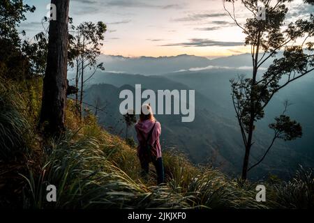 A young female hiker watching the sunrise over Ella Rock in Sri Lanka Stock Photo