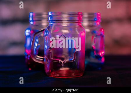 A closeup shallow focus shot of empty gradient color glass jars with a handle on a table Stock Photo