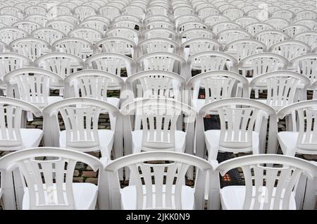 Seemingly endless number of rows of white plastic chairs in an outdoor setting Stock Photo