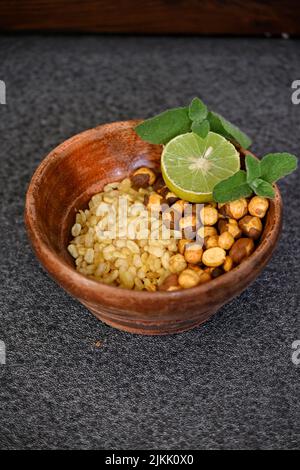 closeup the fried yellow gram split lentils with black gram and sliced lemon ,mint in the red wooden bowl over out of focus grey background. Stock Photo