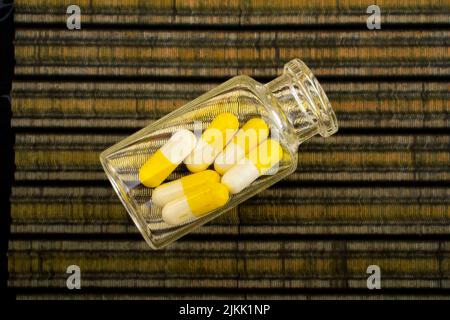 A top view of a transparent bottle filled with yellow and white pills on a striped fabric Stock Photo