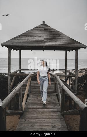 A vertical shot of a young woman walking along a wooden pier against the background of the ocean Stock Photo