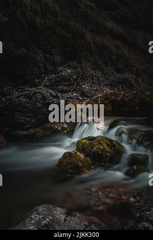 A beautiful vertical shot of a stream flowing through mossy rocky with high hill in the forest Stock Photo