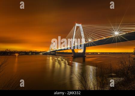 A Vertical shot of a bridge over the water during Sunset and a yellow cloudy sky on the horizon Stock Photo