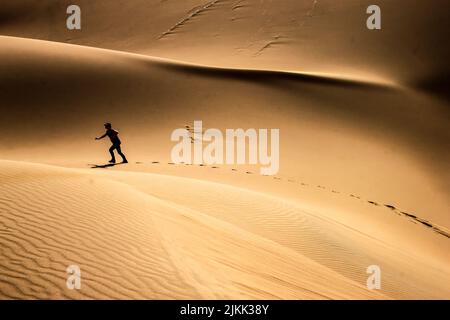A silhouette view of an adult man walking on the sand mounds of Kumtag Desert on a sunny day, Xinjiang , China Stock Photo
