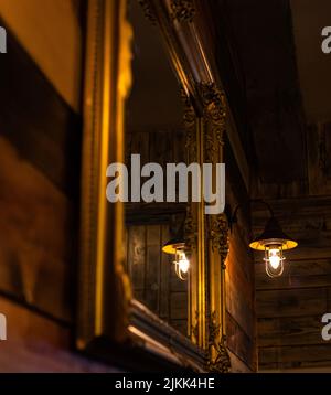 A closeup of a lamp bulb hanging on the wooden wall near a vintage mirror Stock Photo