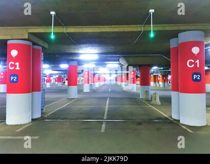 Moscow, Russia, June 2019: Empty underground Parking with colored - red and orange columns, dividing strips for cars and green lights on top, indicati Stock Photo