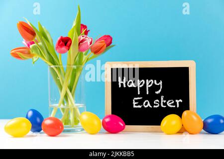 colorful tulips with chalkboard and easter eggs on a blue background with text happy easter Stock Photo