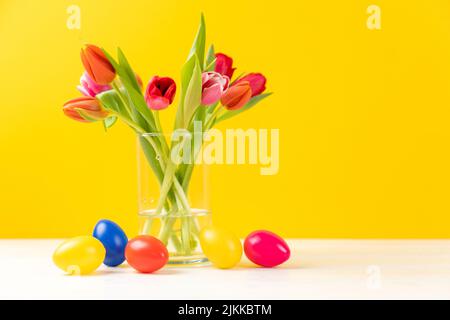 colorful tulips in a vase with colored easter eggs and copy space Stock Photo