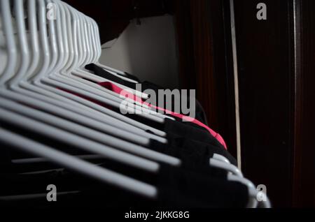 A shot of dark colored clothes hanging on white hangers in a dark closet Stock Photo