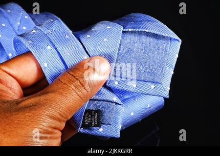 A closeup shot of a male hand showing blue tie with white dots on the black background Stock Photo