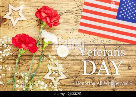 American Veterans Day card with bouquet of carnations, American flag, decoration stars and candles on a wooden background with inscription Veterans da Stock Photo