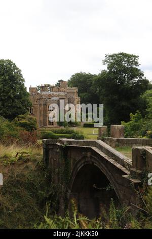 A vertical shot of the stone Hawarden Castle by a bridge in Hawarden, Flintshire, Wales with trees and a gray cloudy sky Stock Photo