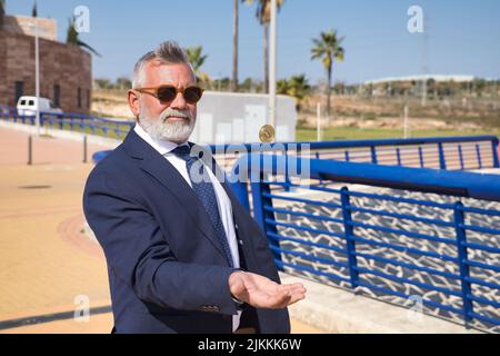 Mature man, executive, gray-haired, bearded, wearing sunglasses, jacket and tie, throwing a cryptocurrency in the air with his hand. Executive concept Stock Photo