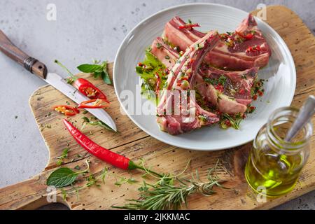 From above of plate with raw lamb chops placed on wooden chopping board with greens and hot pepper in kitchen Stock Photo